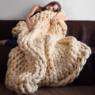 Woman lying on a couch under a large beige knitted blanket