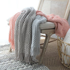 Gray and pink knitted blankets draped over a chair in a cozy room.