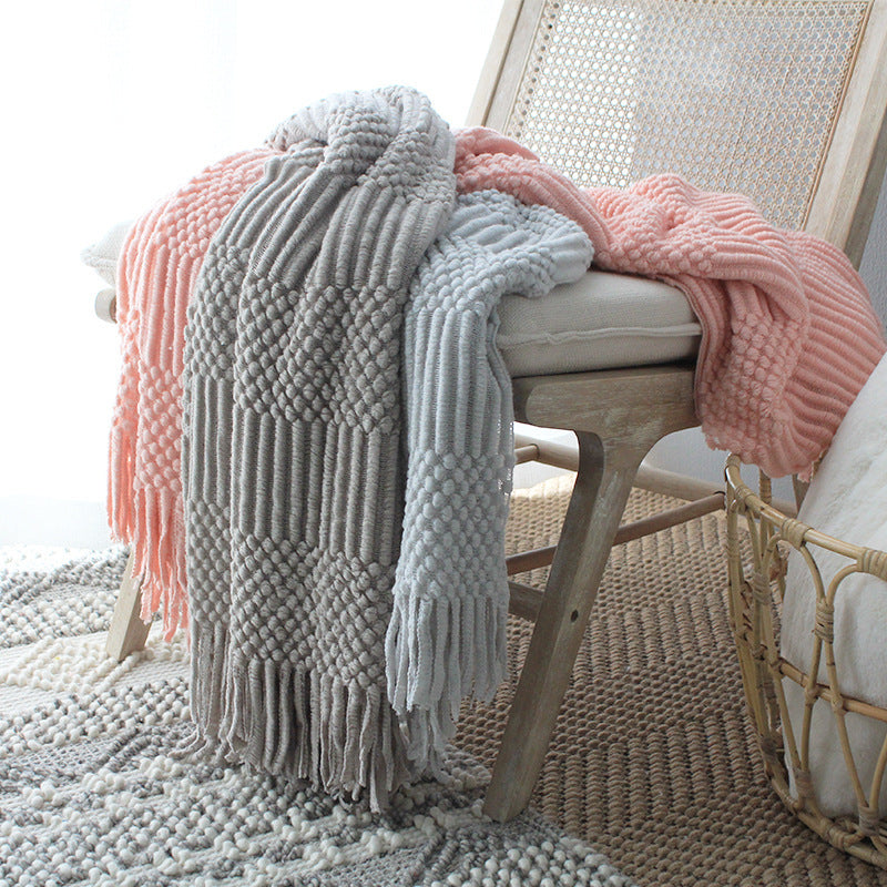 Gray and pink knitted blankets draped over a chair in a cozy room.