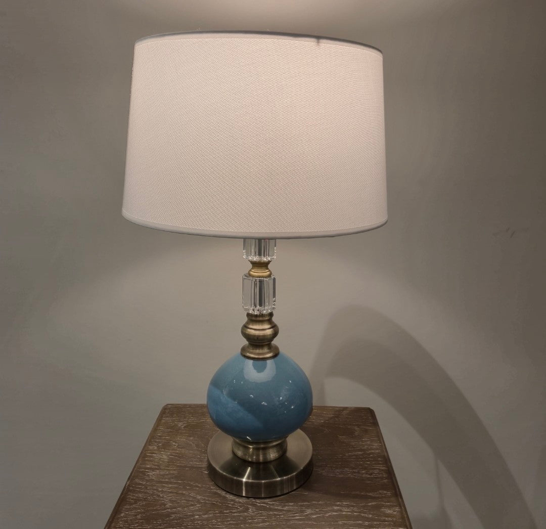 Table lamp with a blue base and white shade on a wooden surface.