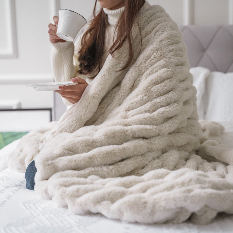 Person wrapped in a cozy beige blanket holding a cup on a bed.