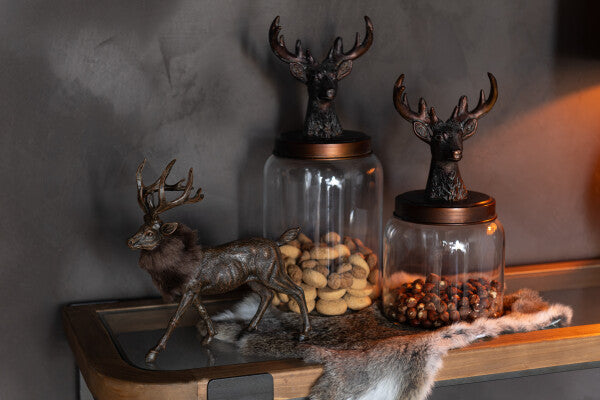 Decorative jars with deer heads on a shelf against a dark wall.