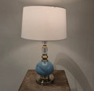 Table lamp with a blue base and white shade on a wooden surface.